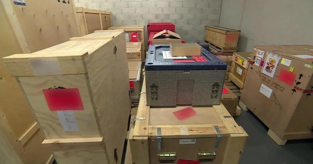 A storeroom stacked with sealed plywood shipping crates of different sizes, each carrying red and white paperwork labels.