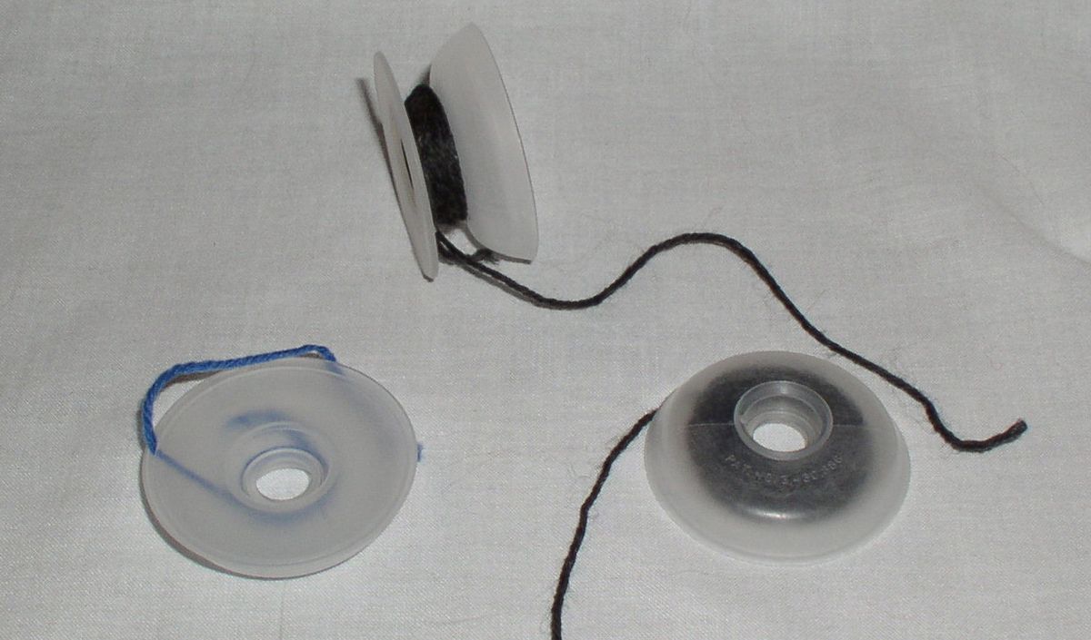 Three small wound bobbins of coloured yarn of the kind used for intarsia knitting, resting on a plain surface.