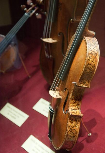 A Stradivarius violin displayed on a stand, its varnished maple back and scroll visible against a dark ground.