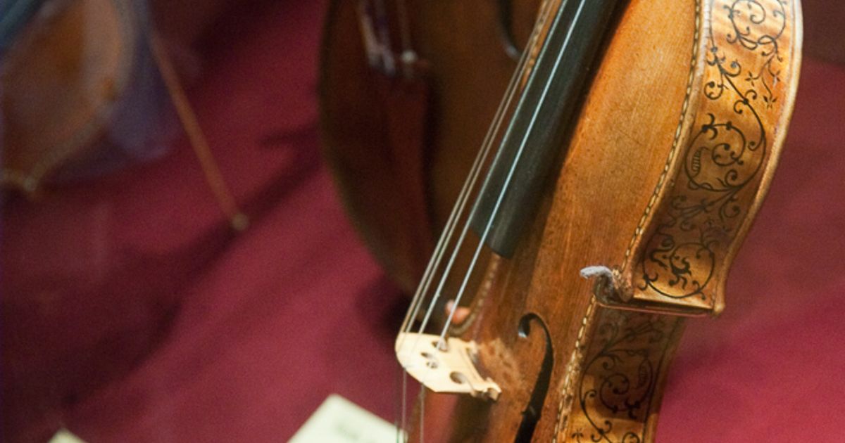 A Stradivarius violin displayed on a stand, its varnished maple back and scroll visible against a dark ground.