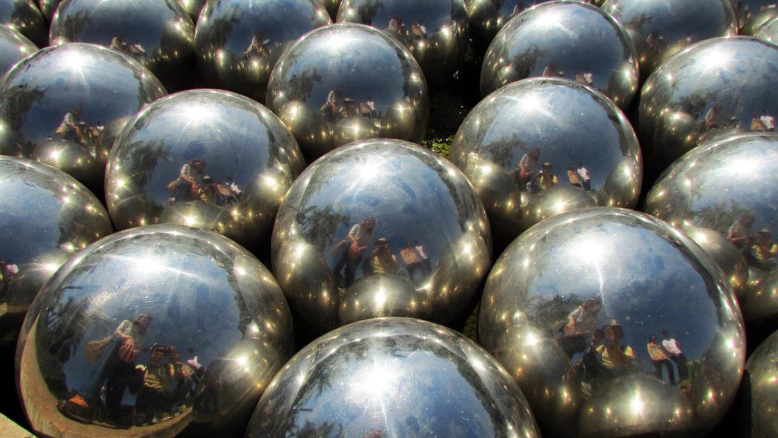 Dozens of mirrored steel spheres packed together, each reflecting visitors standing around them.