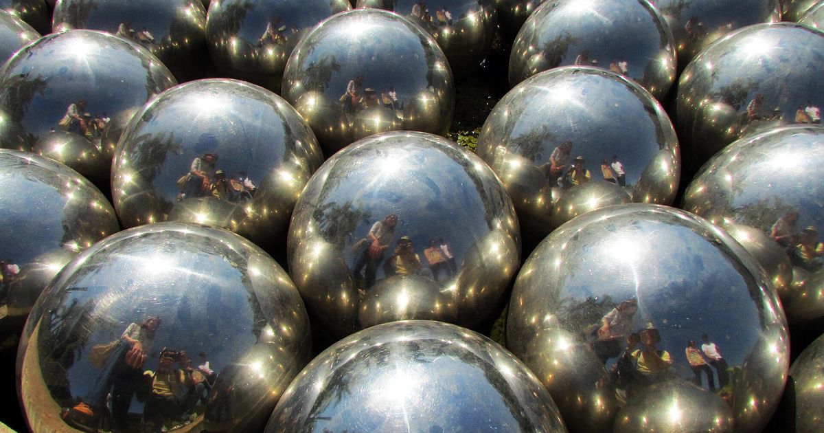 Dozens of mirrored steel spheres packed together, each reflecting visitors standing around them.