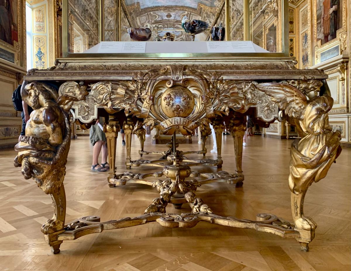 A glass display case in the Galerie d'Apollon at the Louvre, holding objects on dark velvet.