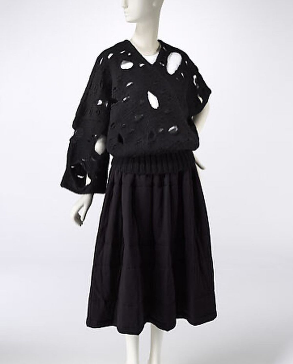 A mannequin in a black knitted sweater pierced with large irregular holes, worn over a full gathered black skirt.