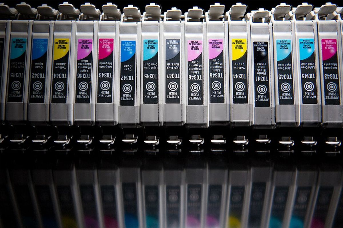 A row of inkjet printer cartridges standing on a reflective black surface. Part numbers are visible; no manufacturer logo is legible.