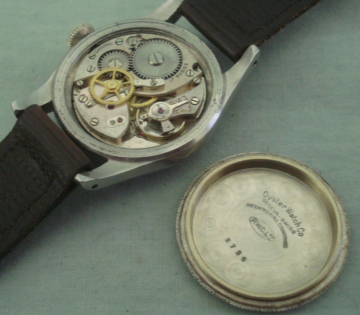 An opened wristwatch with its caseback laid beside it, a case number stamped on the inside of the back and legible in the frame.