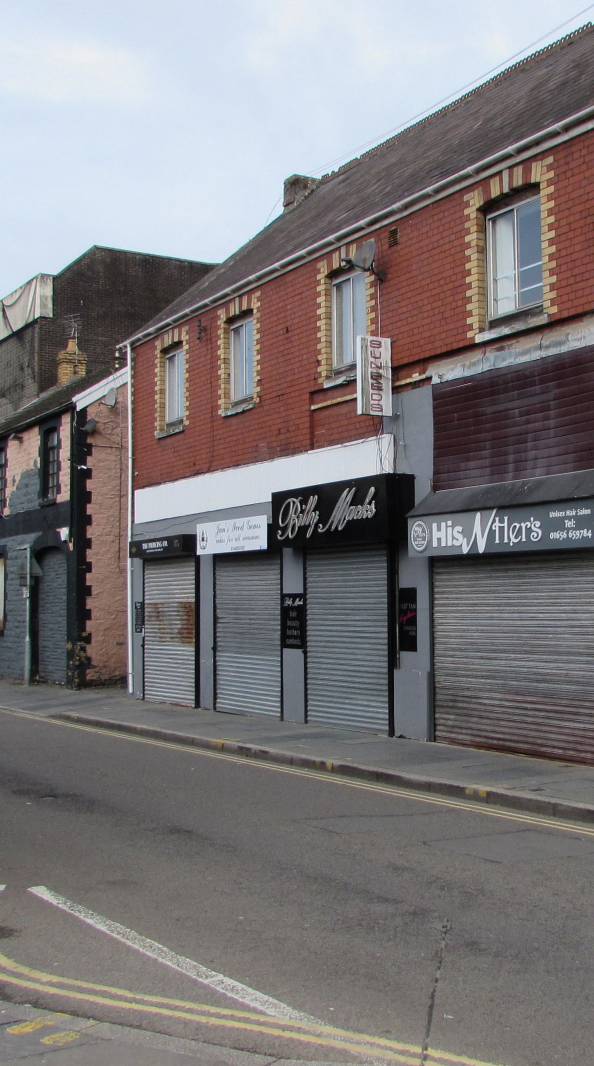 A narrow shopping street with every shopfront closed behind metal roller shutters.