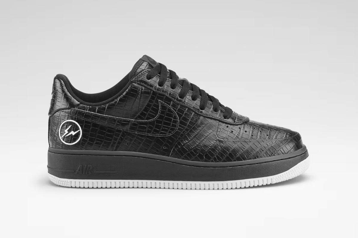 A black leather low top sneaker with a crocodile embossed upper and a white sole, photographed side on against dark grey.