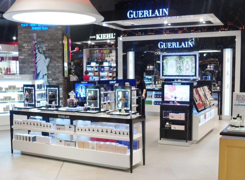 A luxury fragrance counter in an airport duty-free hall, illuminated displays of perfume bottles and branded packaging.