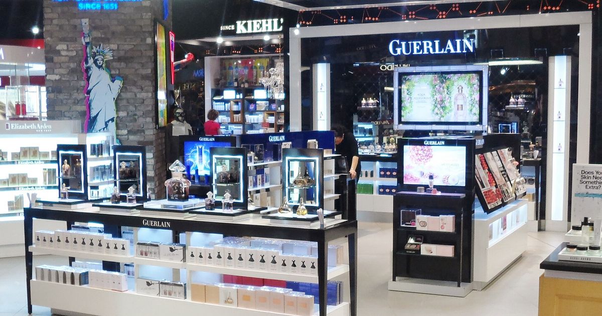 A luxury fragrance counter in an airport duty-free hall, illuminated displays of perfume bottles and branded packaging.