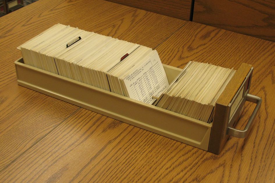 Rows of wooden card catalogue drawers with brass label holders, holding typed index cards.