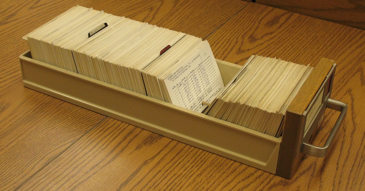 Rows of wooden card catalogue drawers with brass label holders, holding typed index cards.