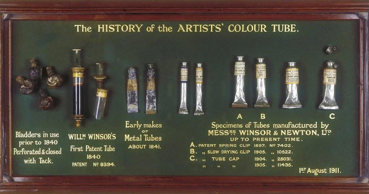 A framed museum display titled The History of the Artists Colour Tube, holding a row of early paint bladders and metal tubes above printed explanatory text.
