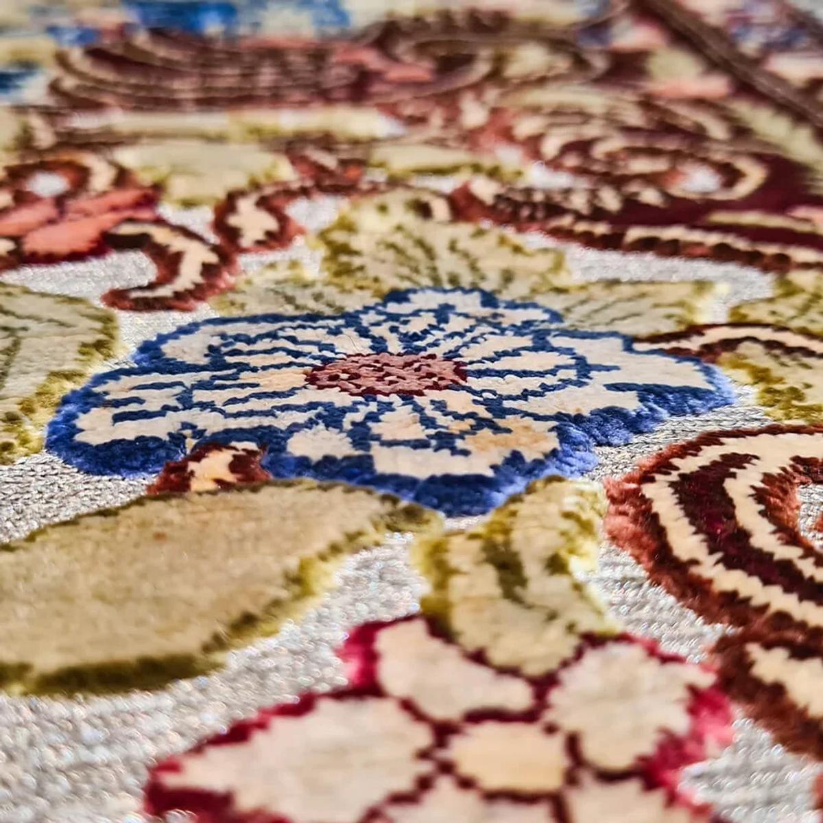 A close view of woven silk showing a large blue and cream flower motif surrounded by dense red, gold and ivory scrollwork.