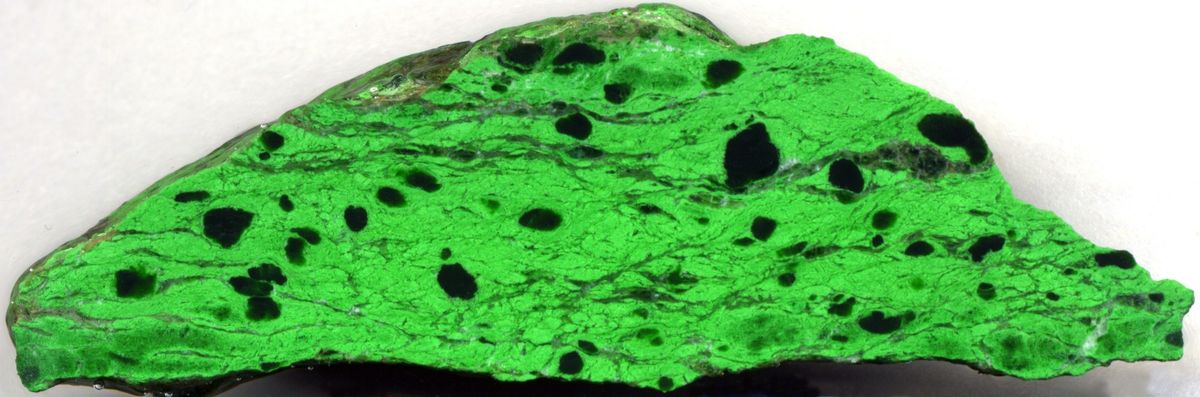 A polished slab of brilliant green rock with black patches.