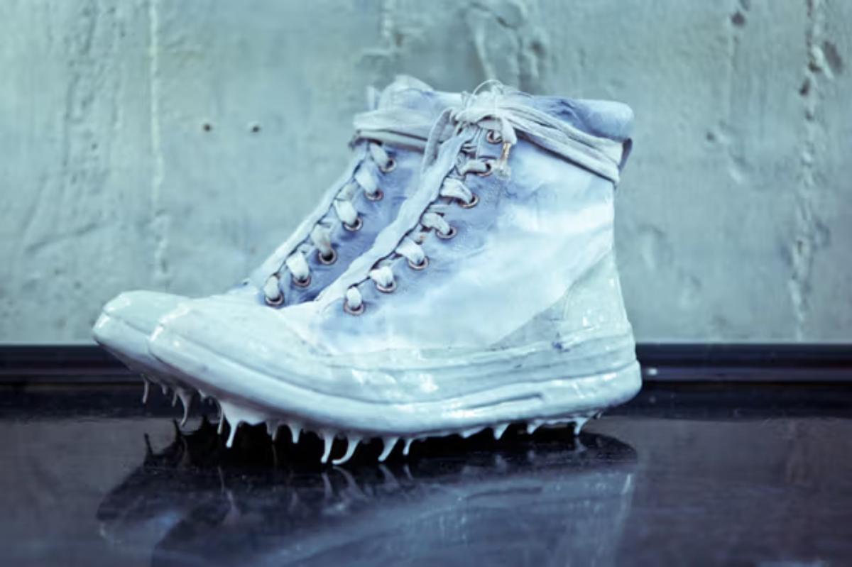 A white high top sneaker photographed against a pale wall, thick white liquid running down its sides and pooling under the sole.