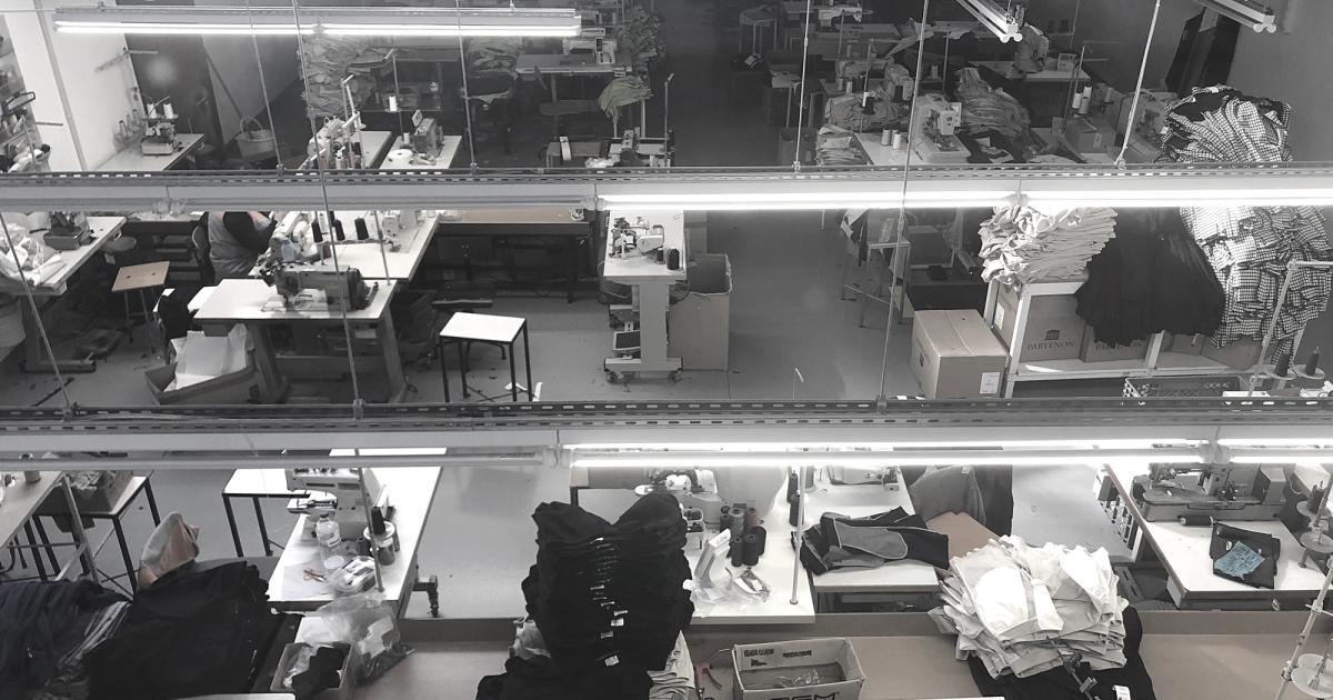 A garment factory floor in Portugal seen from above, rows of sewing stations under strip lights with stacks of identical cut pieces beside each machine.