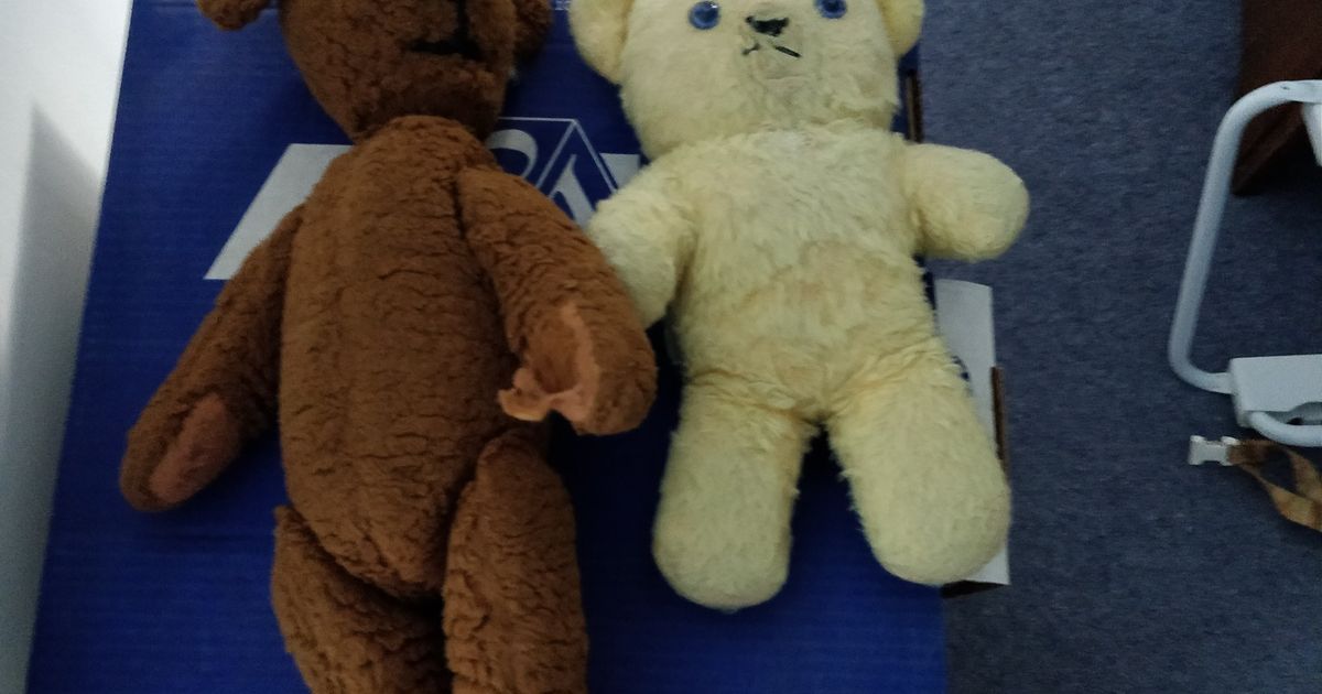 Two old teddy bears with worn, flattened fur and faded stitching, seated side by side.