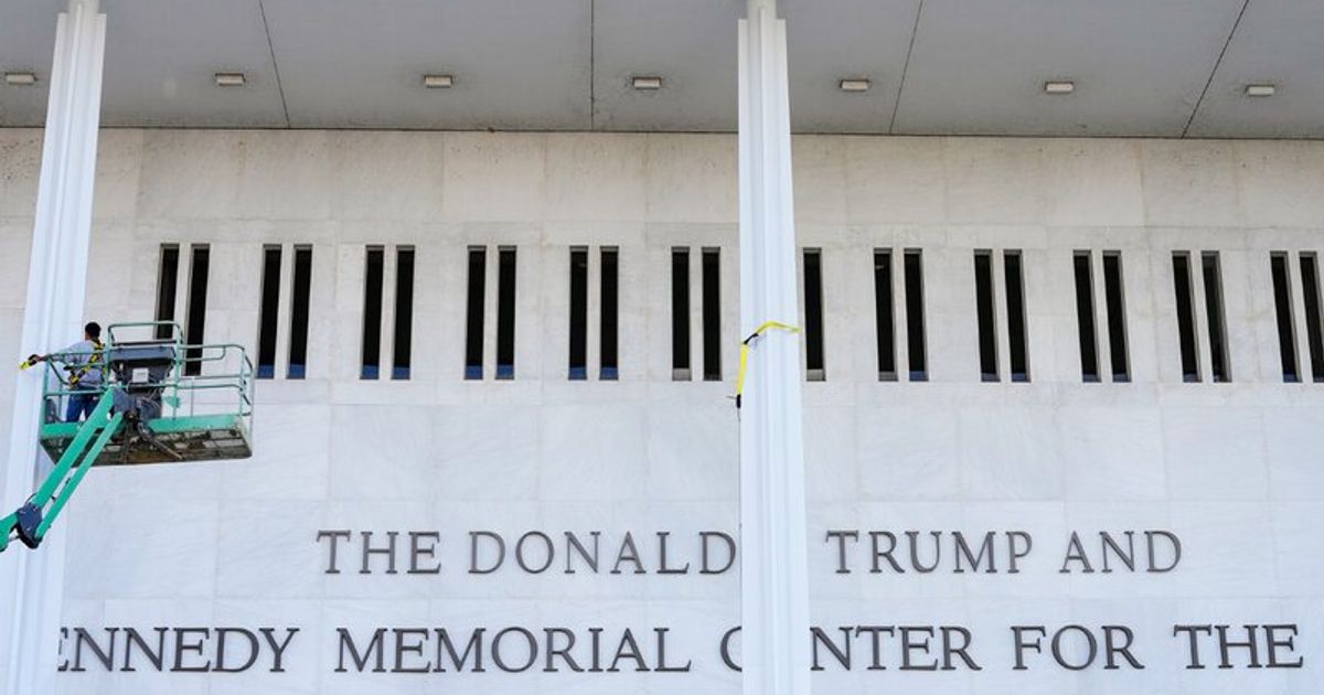 A pale stone building facade under work, a section of giant painted piano keys above carved lettering reading The Donald Trump and Kennedy Memorial Center, with a lift platform in front.