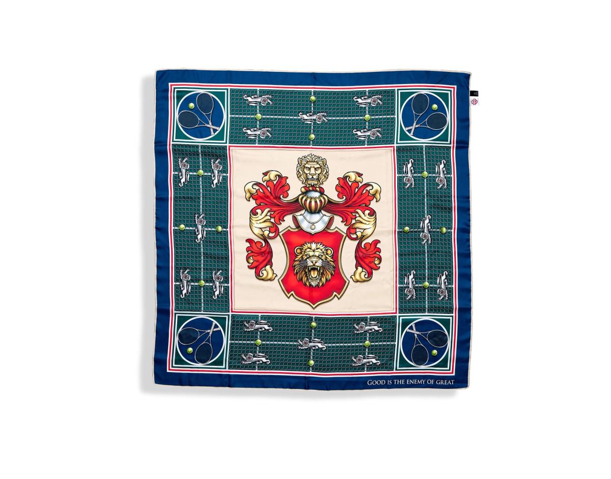 The Court of Tenacity scarf laid flat, a red and gold lion crest at the centre on cream, framed by a green tennis court ground and a navy border.