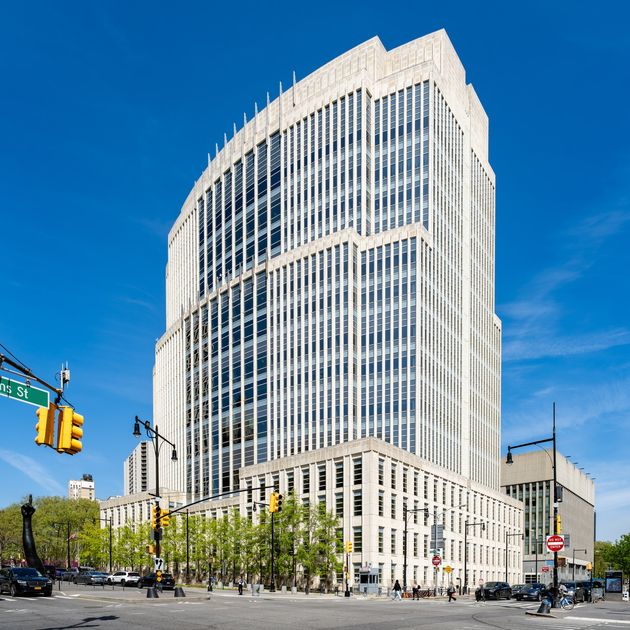 A large pale stone and glass federal courthouse tower seen from a street corner under a clear blue sky.