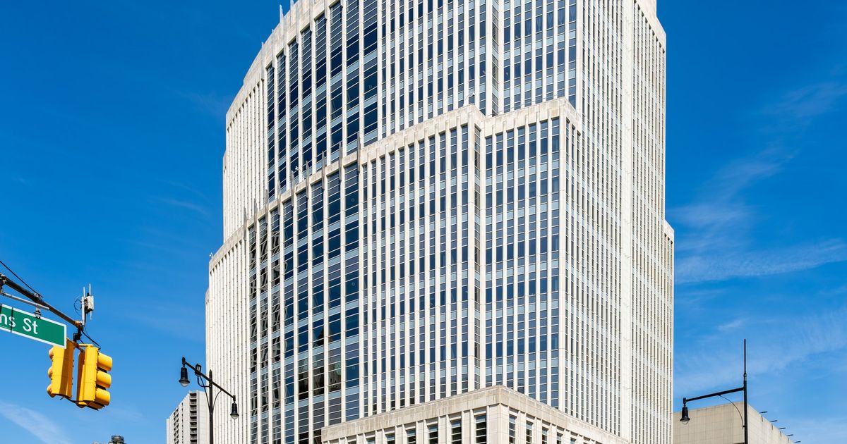 A large pale stone and glass federal courthouse tower seen from a street corner under a clear blue sky.