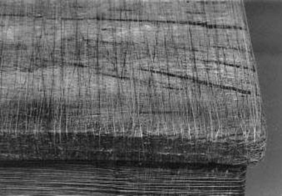 A black and white close view of a dense block of compressed layered material, its cut edge showing fine horizontal striations.