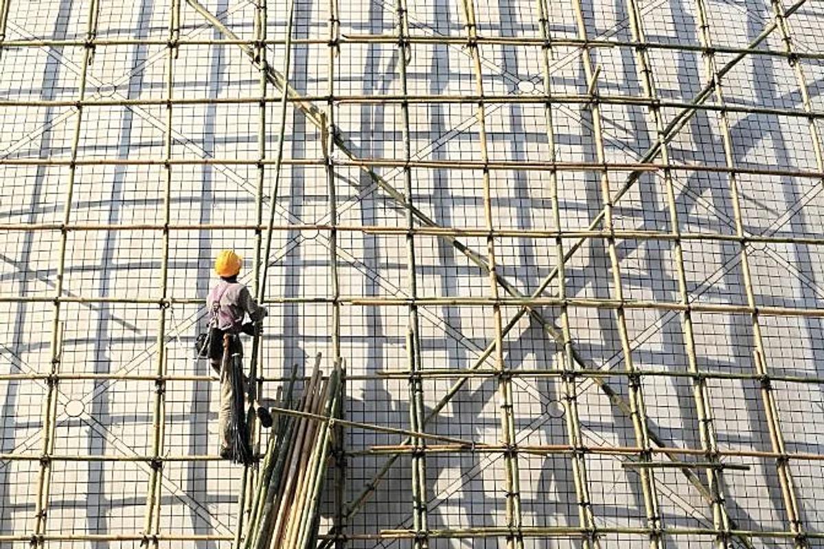 A worker in a yellow helmet climbing a dense lattice of bamboo scaffolding that fills the whole frame.