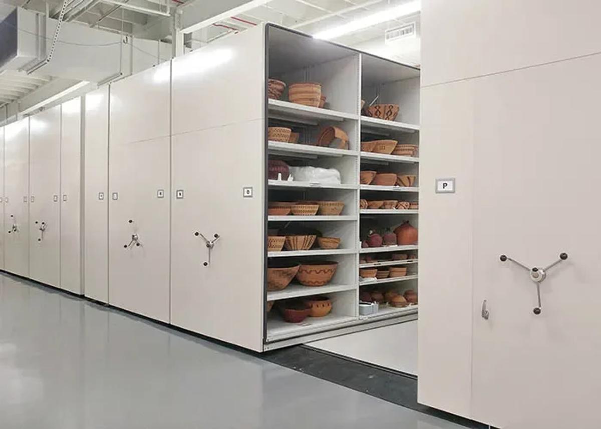 A museum store room lined with white mobile shelving racks holding rows of terracotta vessels on open shelves.