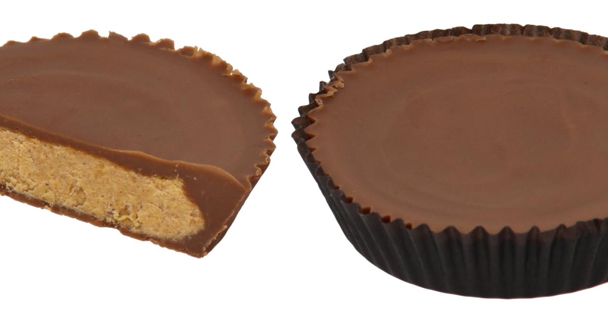 Two peanut butter cups on a plain background, one still in its fluted paper wrapper and the other split in half to show the filling.