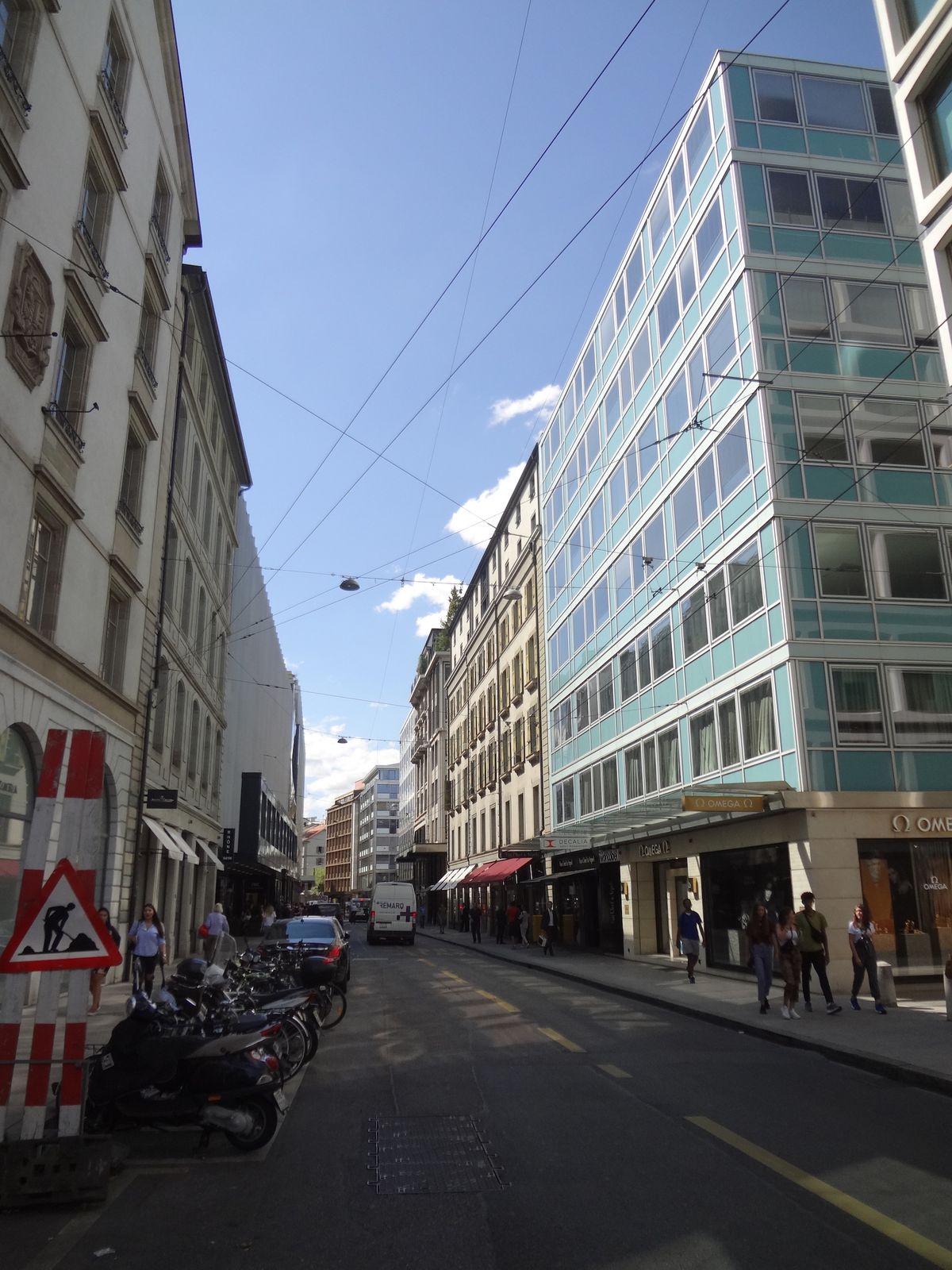 A view west along the Rue du Rhone in Geneva, watch boutiques along the street under a grey sky.