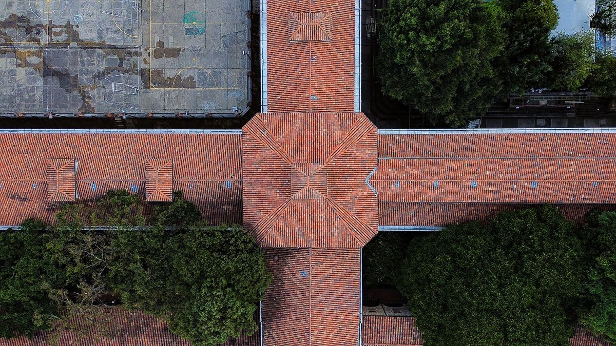 A straight down aerial view of a terracotta tiled roof forming a cross, with an octagonal crossing at its centre and trees on either side.