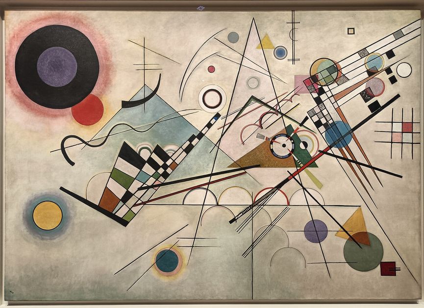 A large abstract canvas on a pale ground covered with circles, triangles, grids and long ruled lines in black, blue, yellow and red.