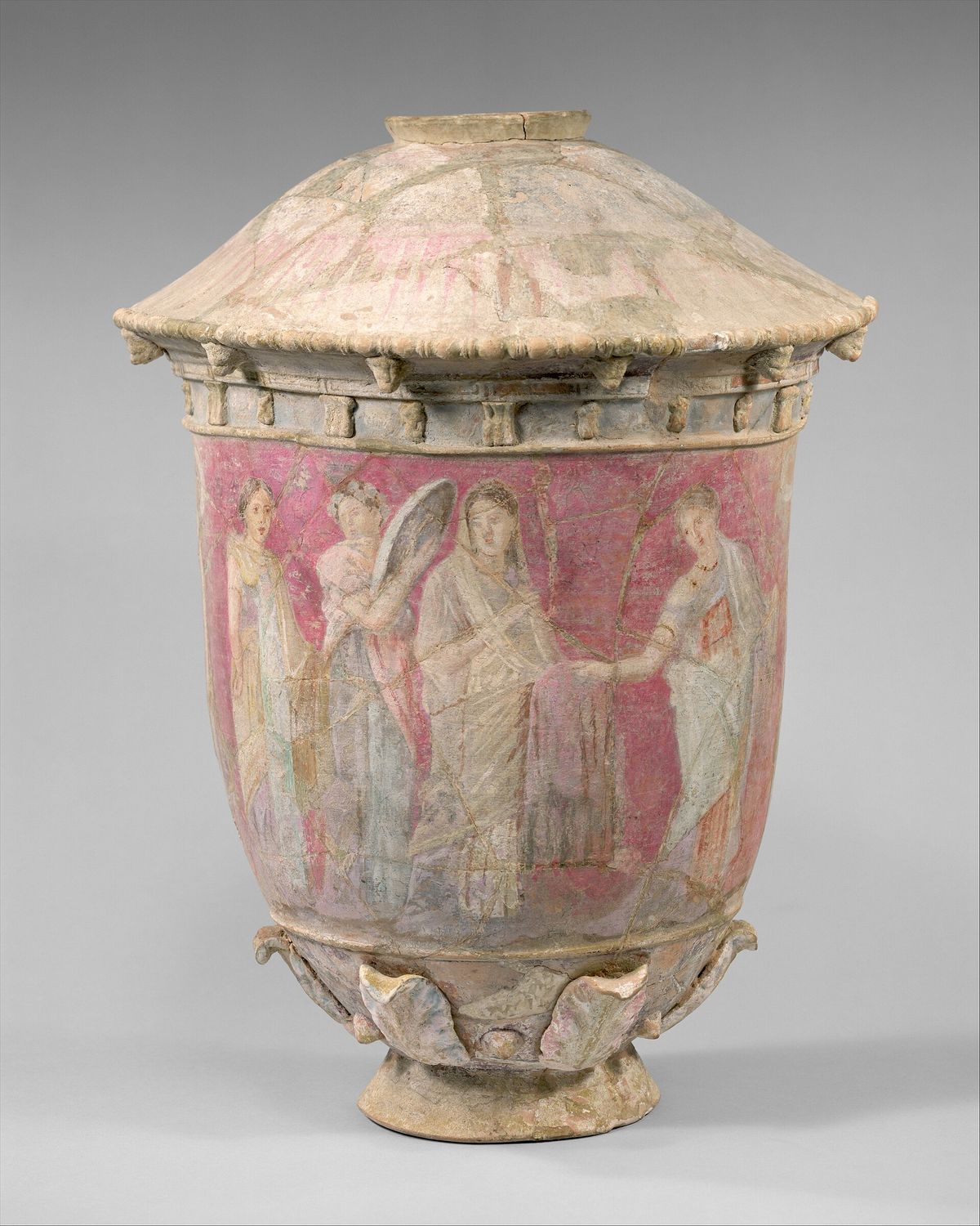 An intact lidded ceramic vase with a conical lid and a pink painted band showing draped figures including a veiled bride.