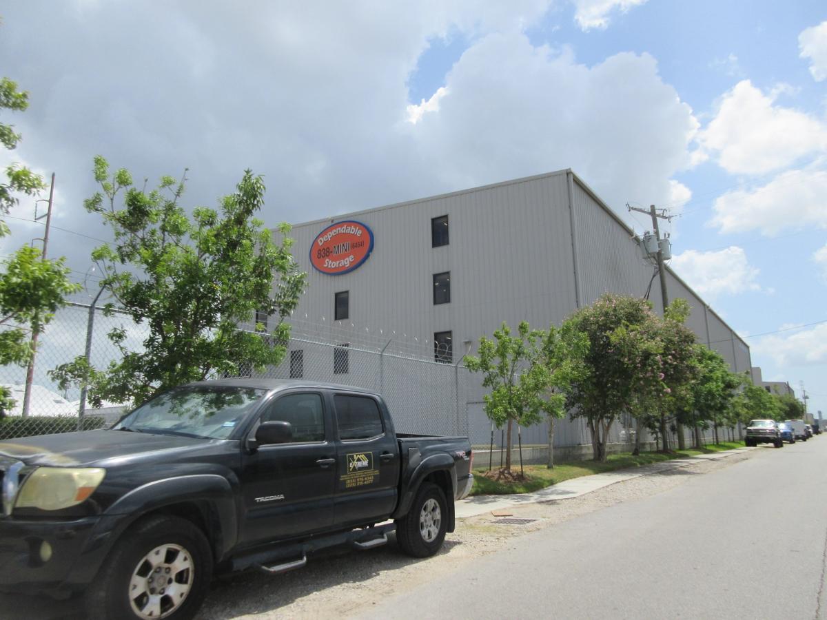 A single storey self storage facility seen from the street, its numbered orange doors facing a parking apron.