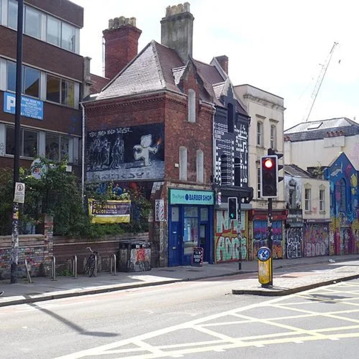 A street corner of brick and rendered buildings covered in graffiti, a barber shop at ground level and a crane on the skyline.