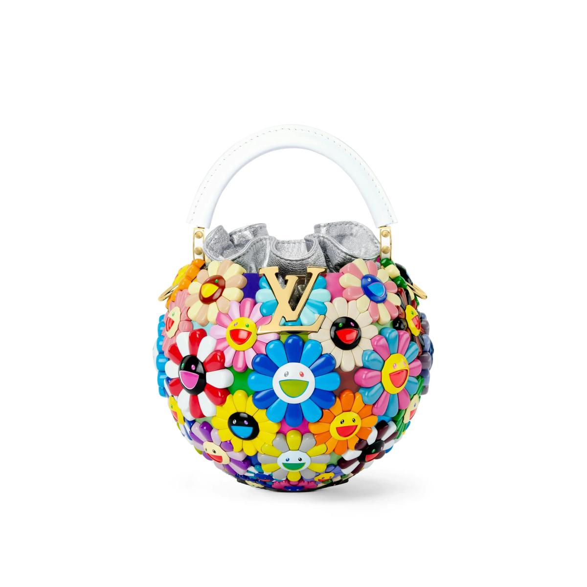 A round handbag covered in dense three dimensional daisies in many colours, each with a smiling face at its centre, with a white top handle and a monogram plate.
