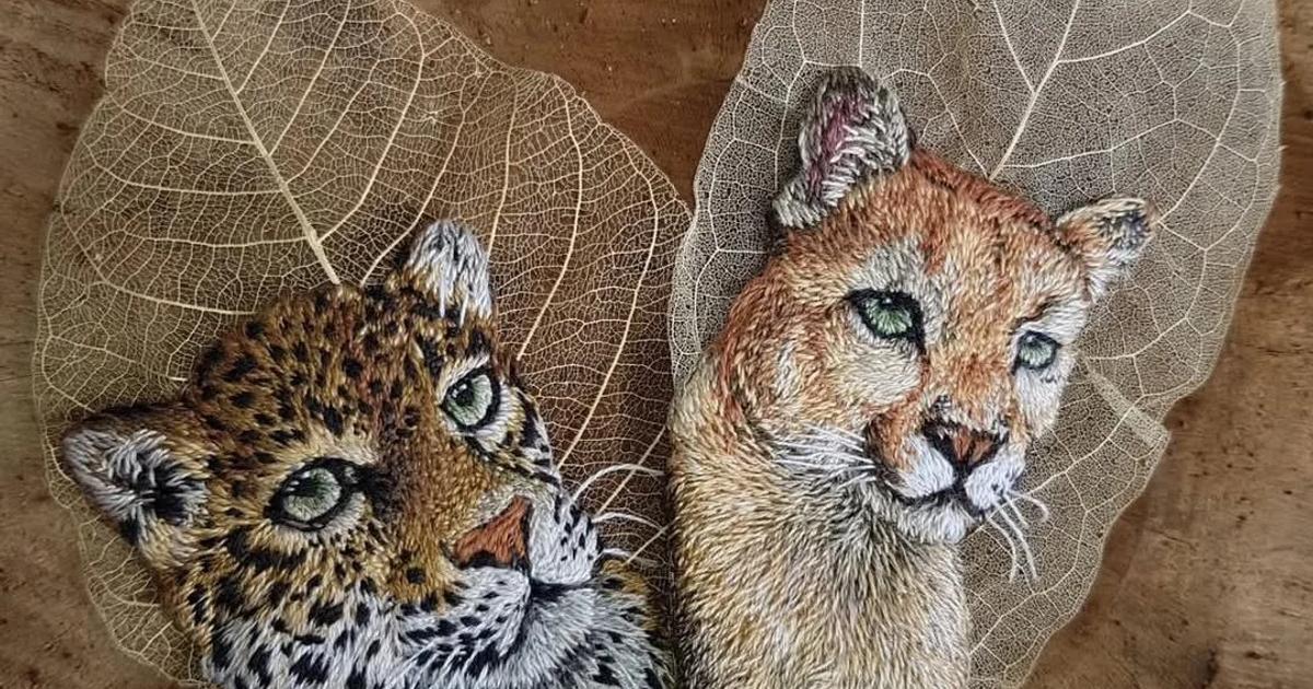 Two skeleton leaves laid on weathered wood, each painted with the head of a big cat, a spotted leopard on the left and a tawny cougar on the right.