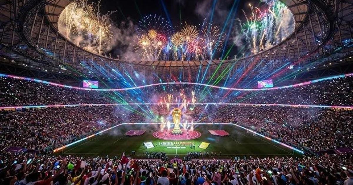 A packed stadium at night during a closing ceremony, fireworks and coloured laser beams above the pitch and a lit stage at the centre of the field.