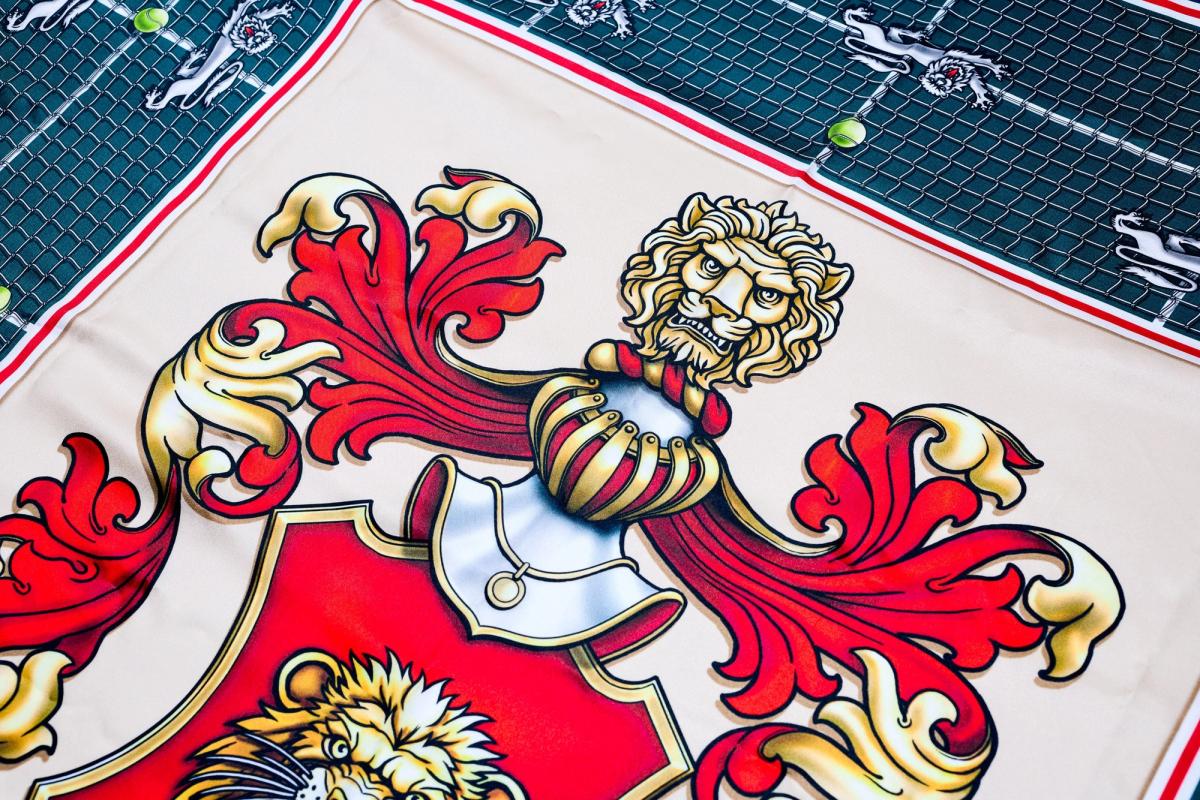 A detail of the scarf's central crest, a red shield with gold and red mantling and a crowned lion, printed on cream against the green court ground.
