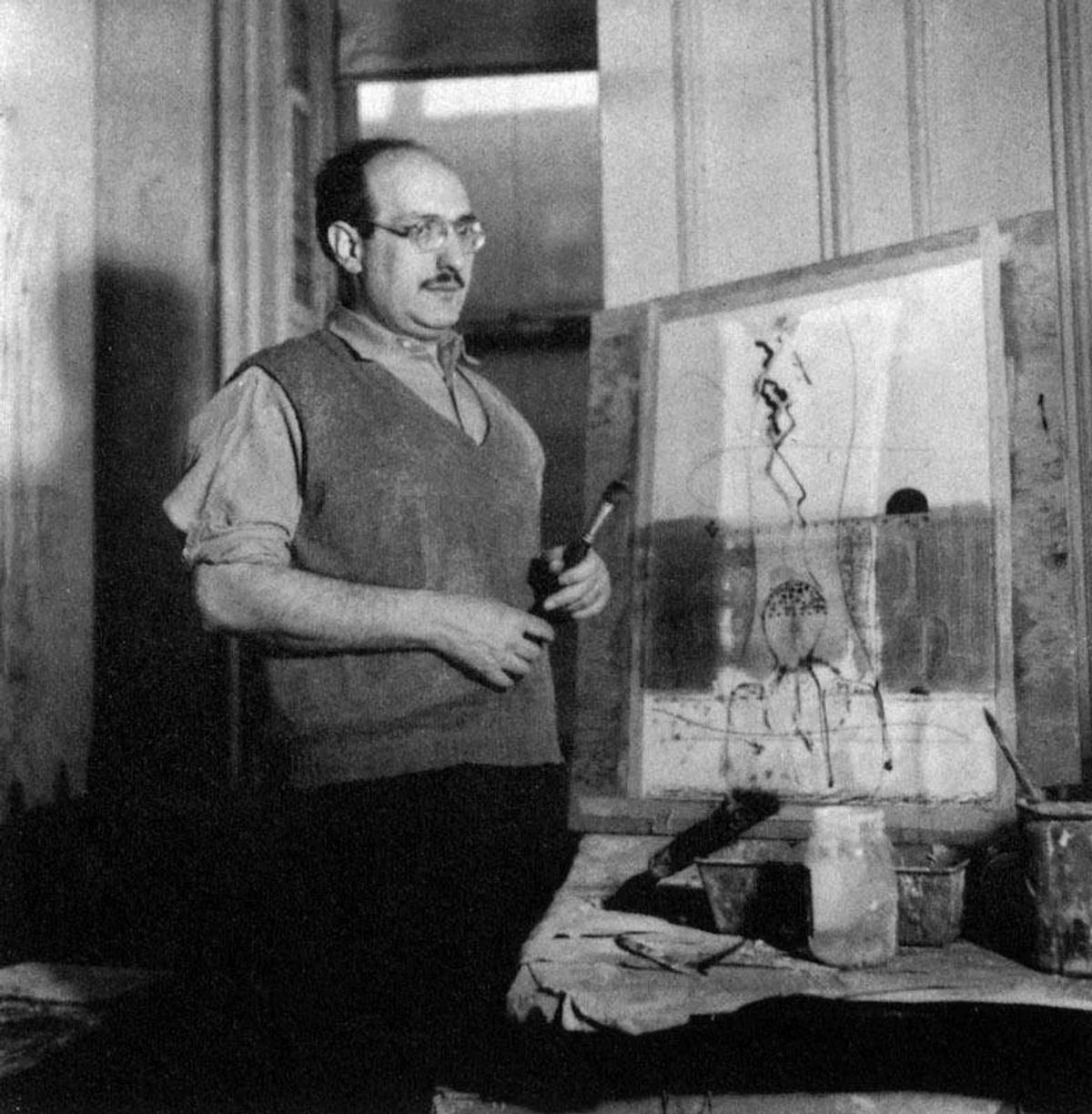 The Artist as Dissenter: A rare black and white photograph of Mark Rothko at work in his studio around the early 1940s. The image captures him during the period of his philosophical dissent, engaged with a canvas that predates his iconic Color Field abstraction. This moment illustrates his core belief that art must serve a profound social and ethical function, setting the stage for his lifelong commitment to P.L.C.F.A. and his custodial strategy of narrative control.