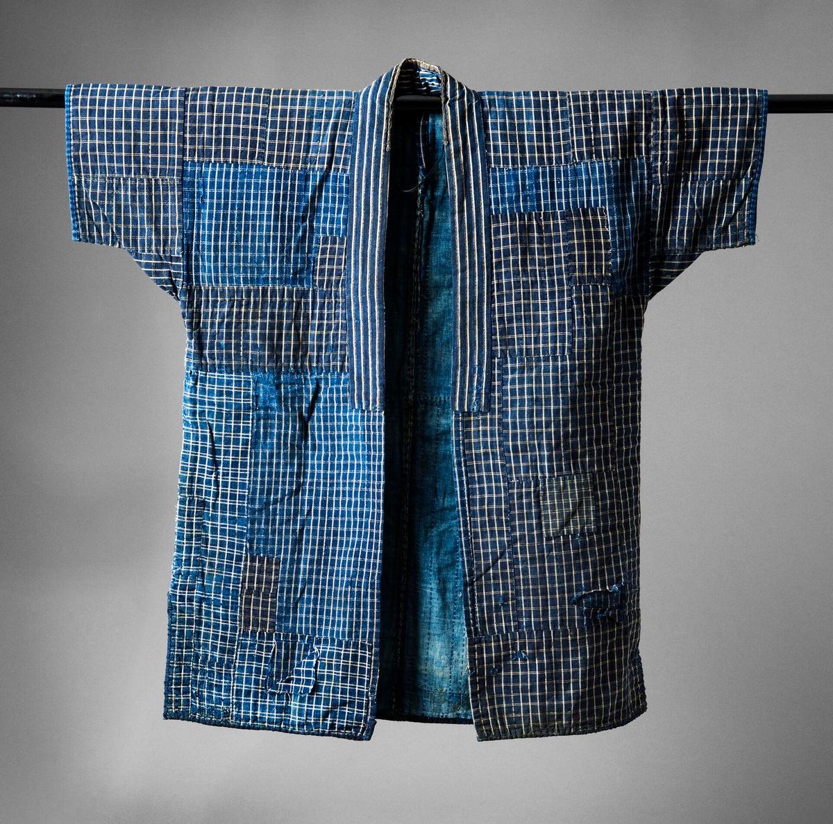 An indigo dyed cotton work jacket laid flat, patched in several tones of blue.