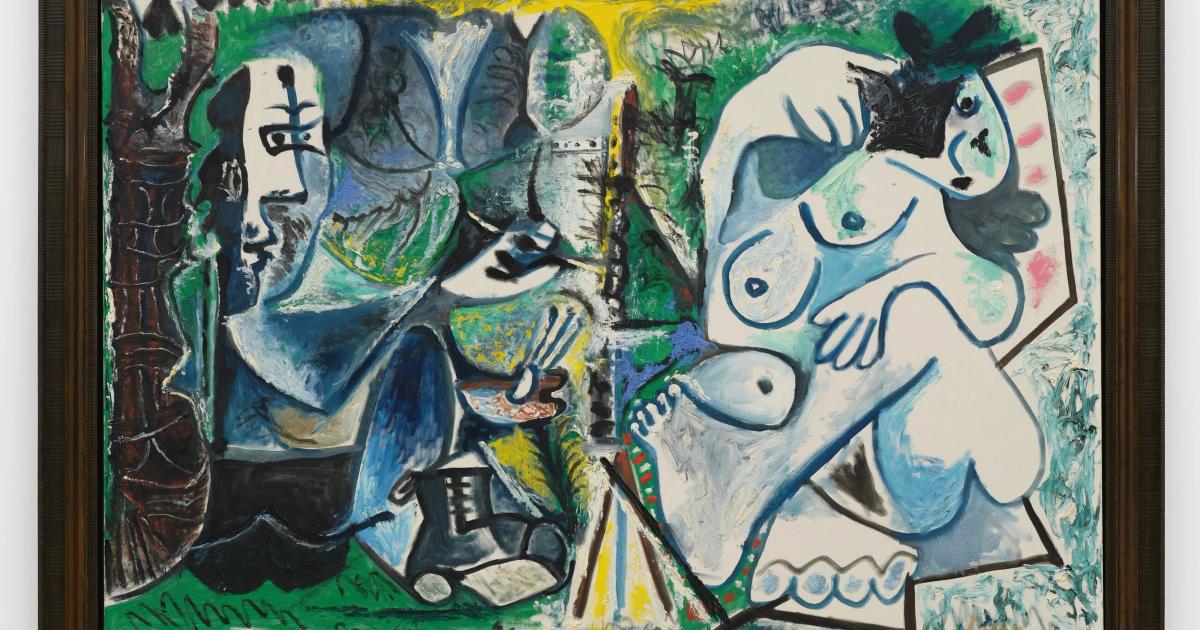 A framed Picasso style painting of two seated figures rendered in blue, green and yellow with fractured faces, hung against a pale wall.