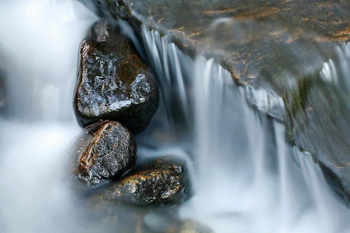 A long exposure photograph of a small waterfall, the water smoothed into white streaks around dark wet boulders.