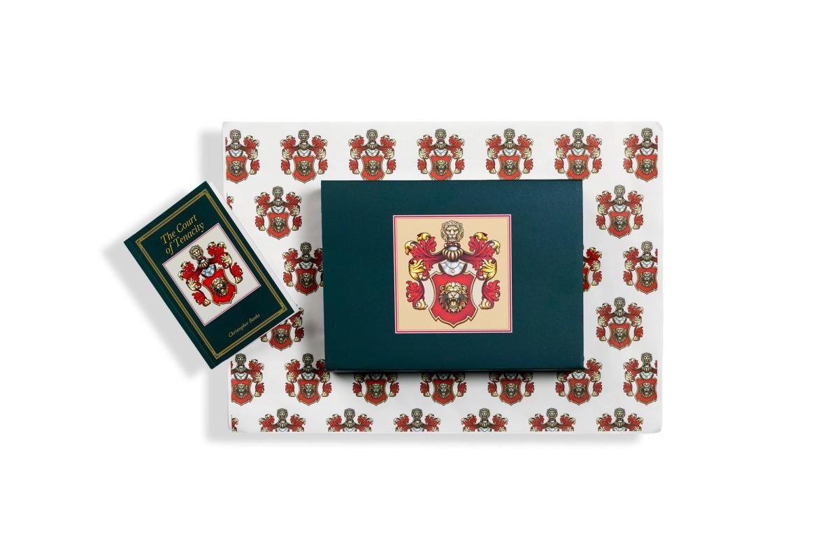 The presentation set seen from above, a small green book beside a mounted crest on dark green board, laid on paper patterned with repeating crests.