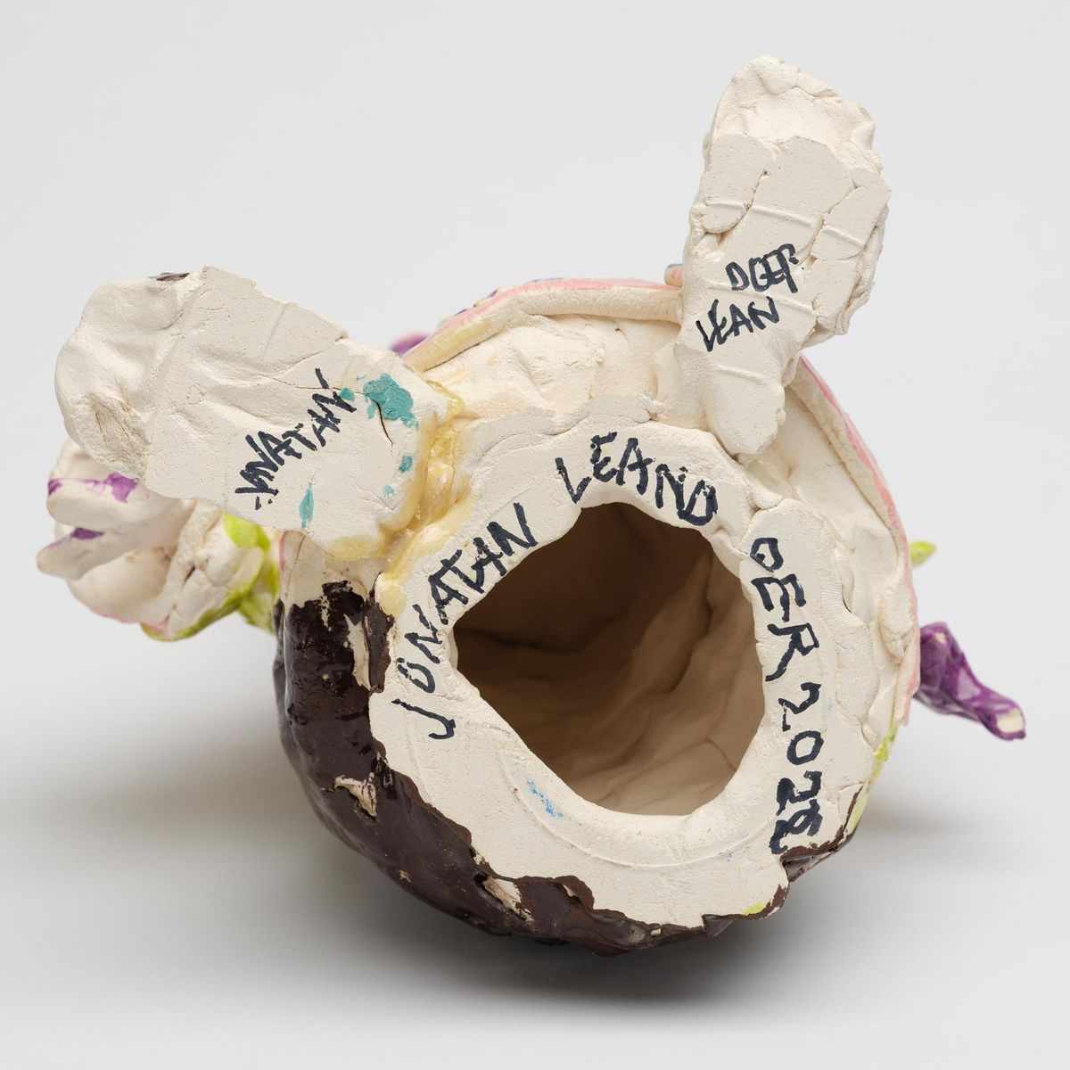 The underside of a glazed ceramic vessel, the opening ringed by unglazed white clay carrying a signature and a date in black marker.