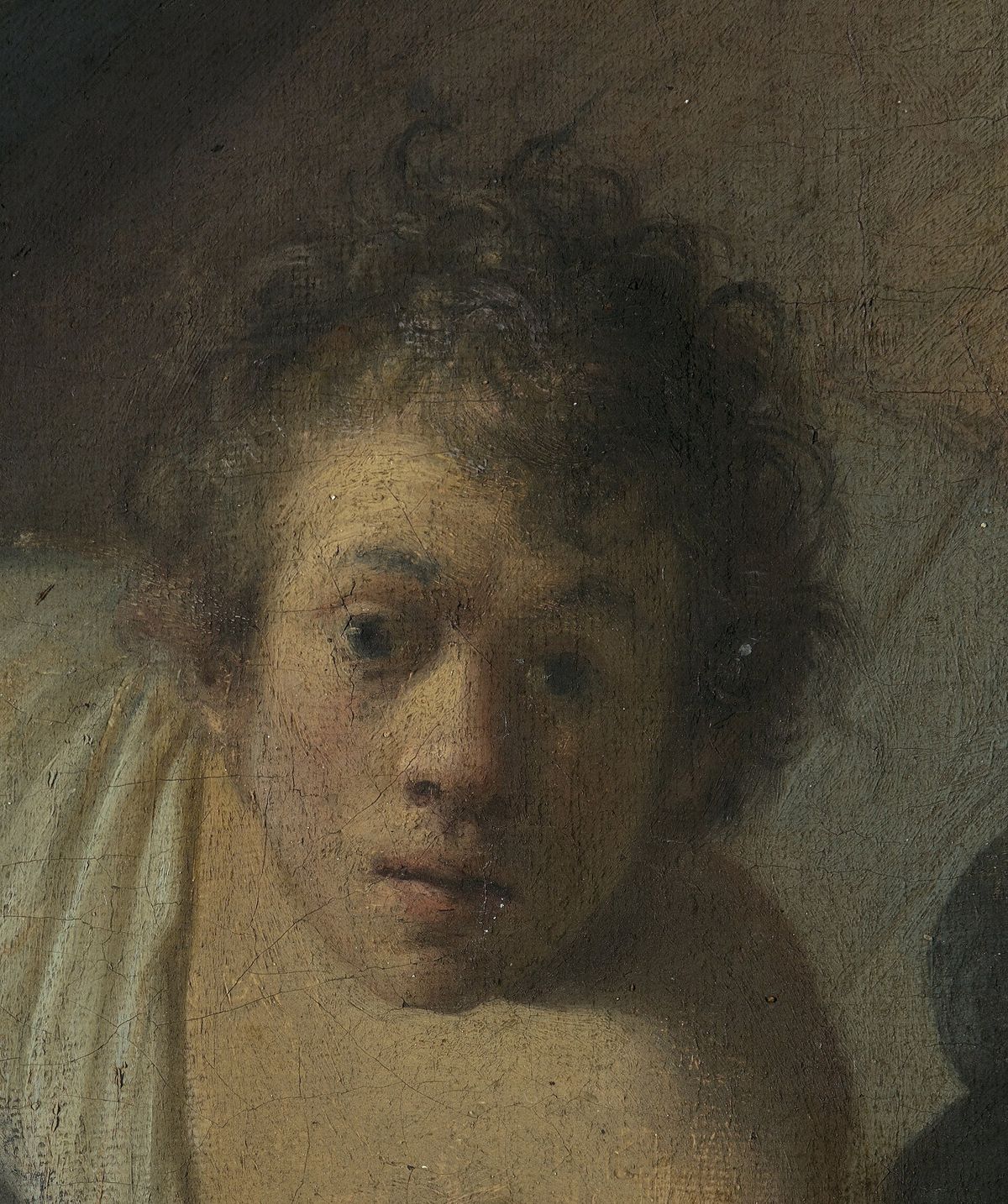A close detail of a young man with thick curling hair and a pale collar, face turned out of the picture toward the viewer.