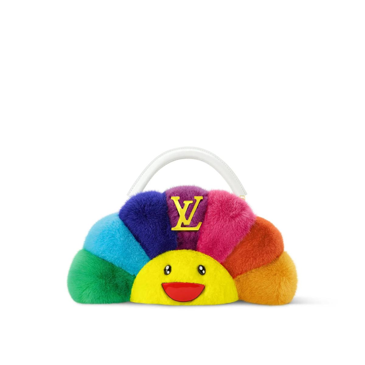 A small handbag whose body is a fan of coloured fur segments, red, blue, green, orange and pink, around a yellow smiling face, with a monogram plate and clear top handle.