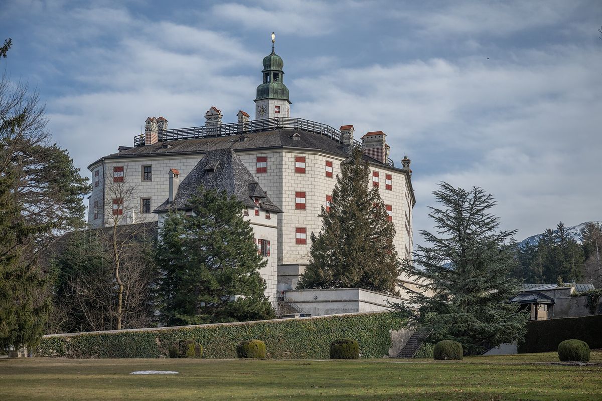 A white Renaissance castle with steep roofs on a wooded hillside, seen from below.