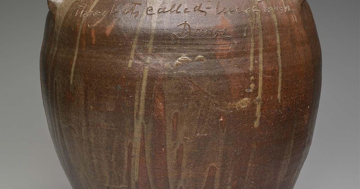 A large brown alkaline-glazed stoneware storage jar with two lug handles, drips of lighter glaze running down its sides, and a line of handwriting incised around the shoulder ending in the name Dave.